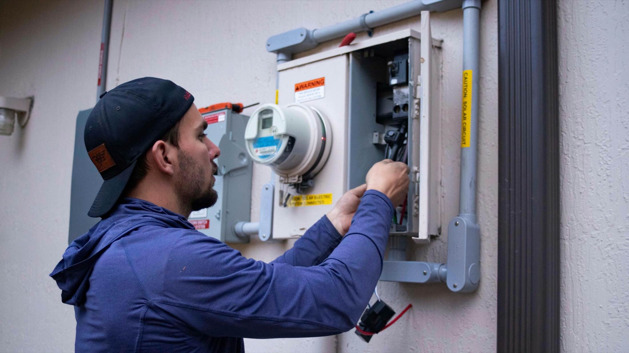 A technician in a cap working at an exterior service panel
